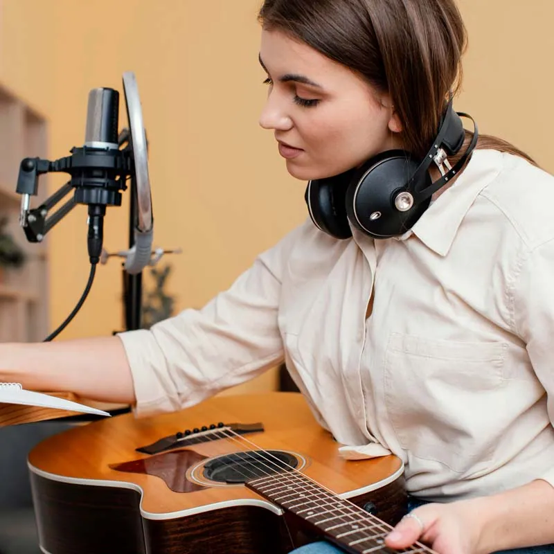 Young woman with headphones playing acoustic guitar in front of a studio microphone