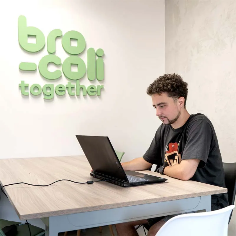 Young man working on a laptop at a table under the green Bro-coli together logo