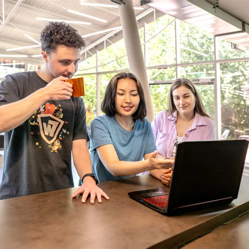 Three young residents looking at a laptop at a counter in a bright glass-walled lounge
