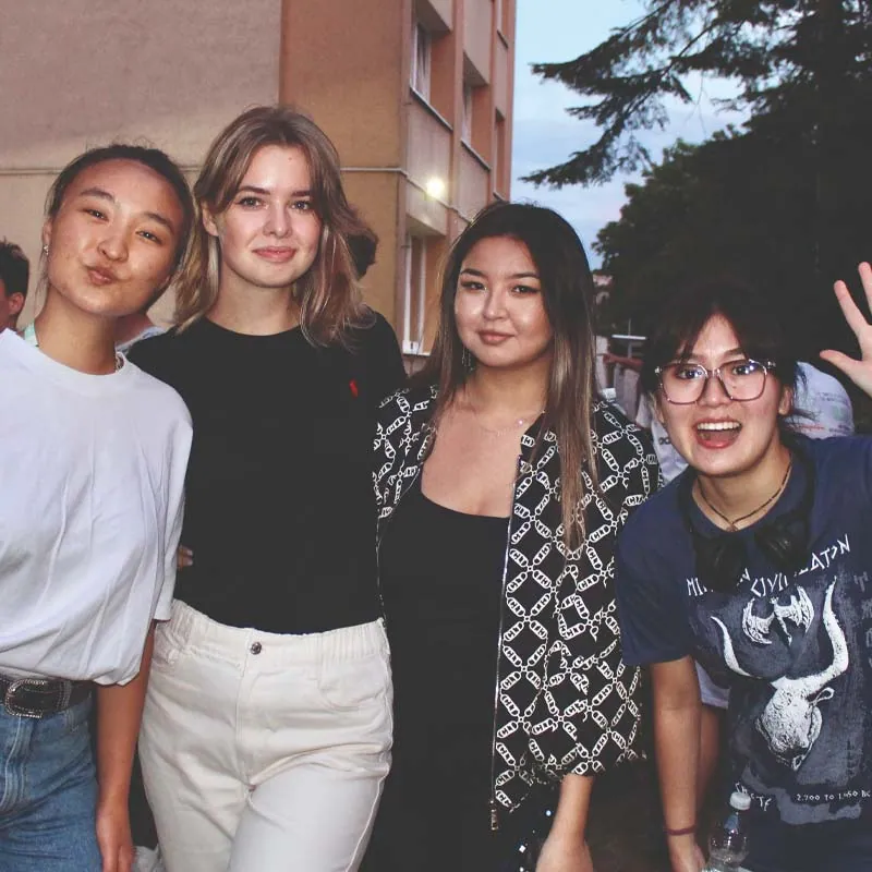 Four young women smiling at the camera outside a residential building in the evening