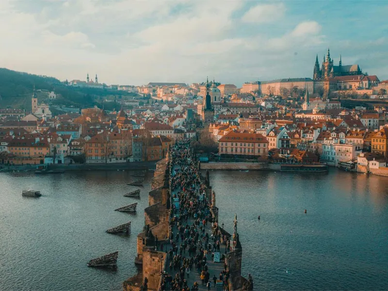 Charles Bridge crowded with people, with Prague Castle above the Vltava at sunset