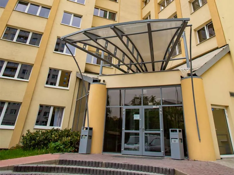 Вход в здание Bro-coli Střížkov со стеклянными дверями под изогнутым козырьком
